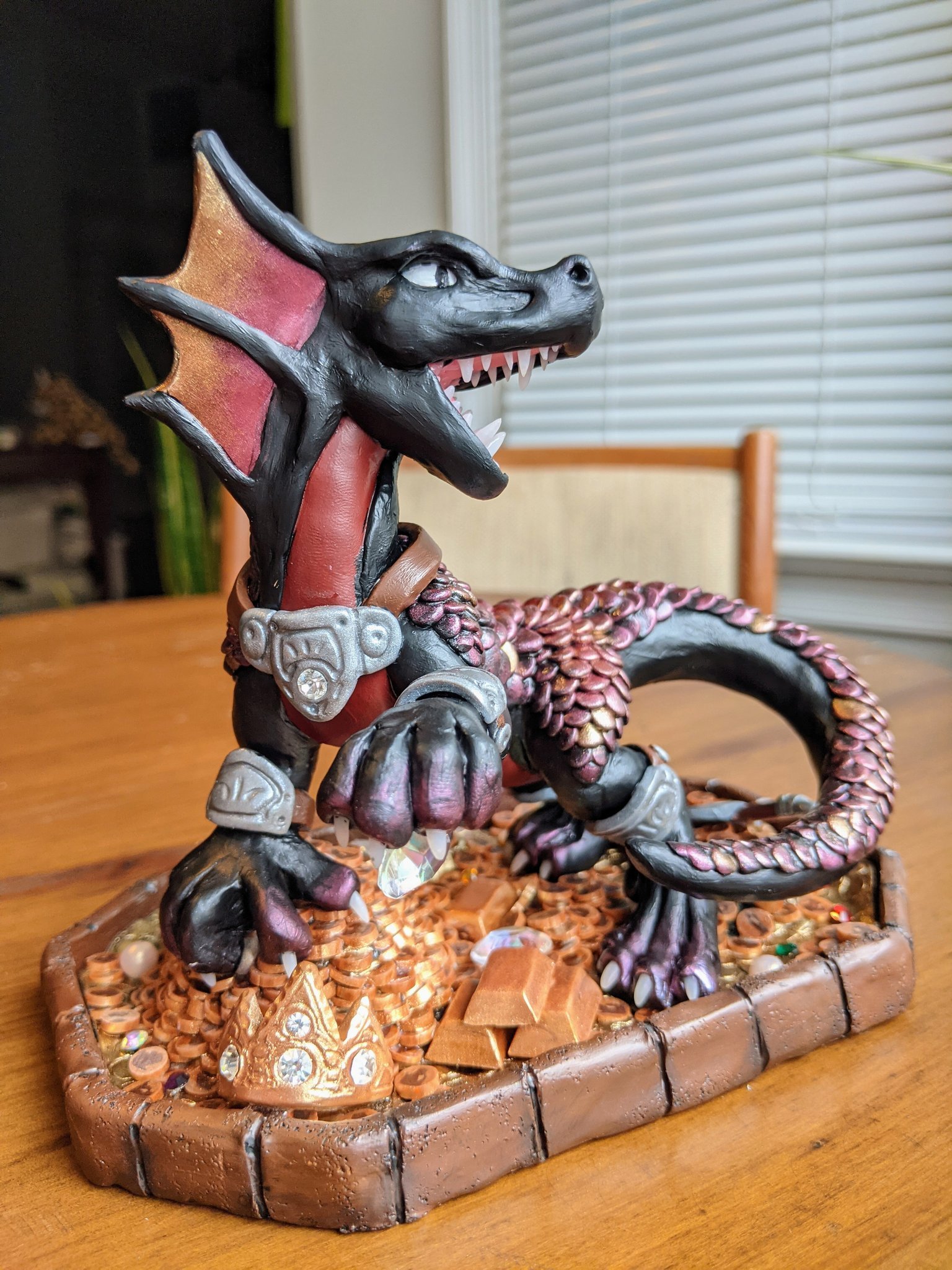 Sculpture of a black and red dragon, standing on a treasure pile of gold coins and gems.